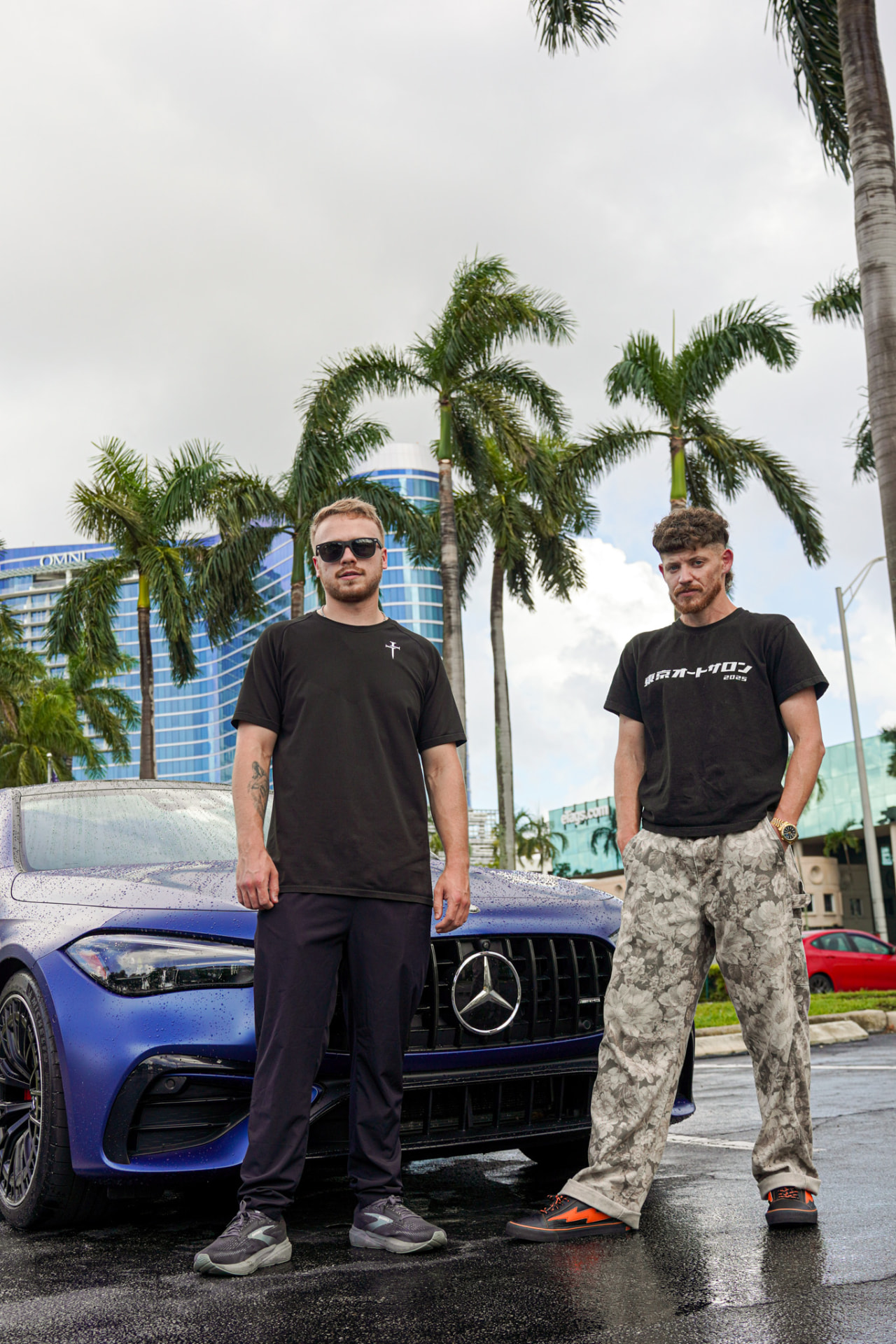Two men posing with a blue Mercedes beneath palm trees
